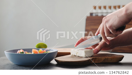 Man cutting feta cheese on olive wood board for greek salad Man cutting feta cheese on olive wood board for greek salad 134762842