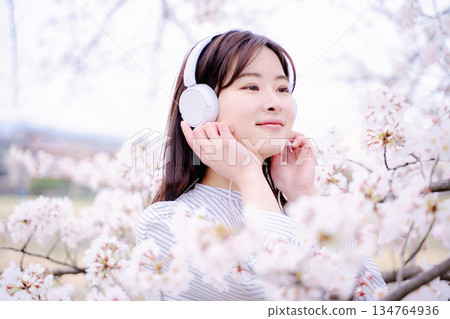 年輕女子在櫻花樹下欣賞音樂 年輕女子在櫻花樹下欣賞音樂 134764936