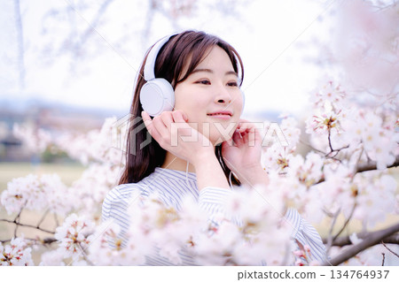 年輕女子在櫻花樹下欣賞音樂 年輕女子在櫻花樹下欣賞音樂 134764937
