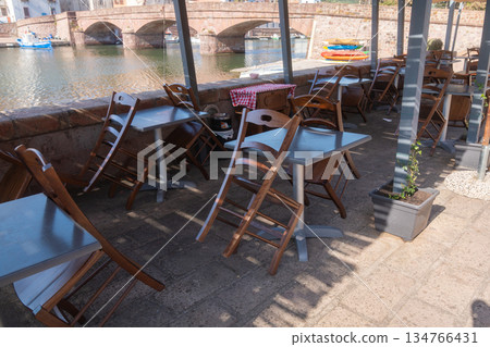 A bright outdoor cafe terrace with simple chairs arranged in warm sunlight. The clean and airy setup suits lifestyle, hospitality and travel themes. 134766431