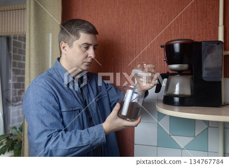Man preparing fresh coffee at home using an electric coffee maker. Casual morning routine in a cozy kitchen, everyday lifestyle, simple domestic moment, authentic home brewing scene. Man preparing fresh coffee at home using an electric coffee maker. Casual morning routine in a cozy kitchen, everyday lifestyle, simple domestic moment, authentic home brewing scene. 134767784