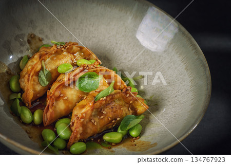 Gourmet Asian Dumplings with Edamame and Sesame Sauce on Dark Background Gourmet Asian Dumplings with Edamame and Sesame Sauce on Dark Background 134767923
