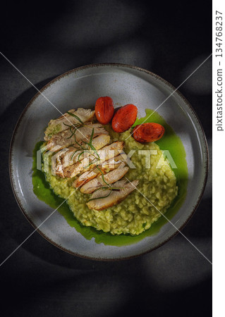 Grilled chicken breast on green pea risotto with roasted cherry tomatoes and rosemary, top view 134768237
