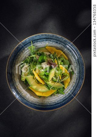 Fresh summer salad with avocado, mango and mixed greens in a blue ceramic bowl, top view Fresh summer salad with avocado, mango and mixed greens in a blue ceramic bowl, top view 134768358