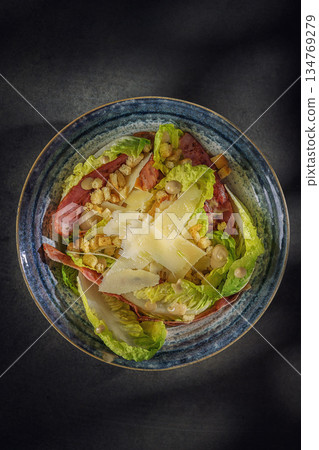 Gourmet Caesar salad with crispy bacon, parmesan shavings and croutons in a blue bowl, top view 134769279