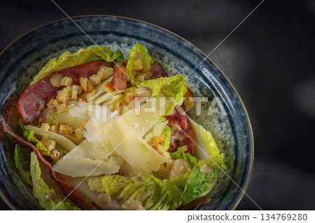 Gourmet Caesar salad with crispy bacon, parmesan shavings and croutons in a blue bowl, top view 134769280