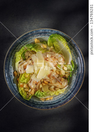 Gourmet Caesar salad with crispy bacon, parmesan shavings and croutons in a blue bowl, top view 134769281