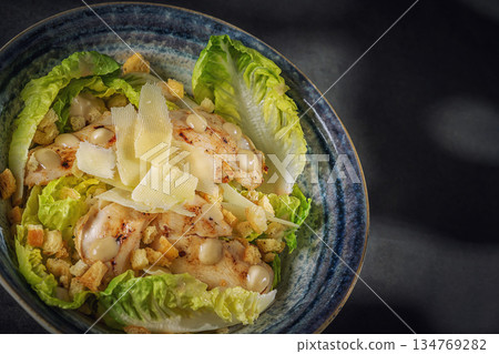 Gourmet Caesar salad with crispy bacon, parmesan shavings and croutons in a blue bowl, top view 134769282