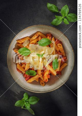 Penne pasta with tomato sauce, fresh basil leaves and parmesan shavings in a rustic bowl 134769526