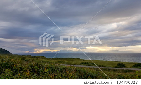 Evening coastal view on the Kuril Islands. Rolling green hills meet the sea under a dramatic sky. Sunlight streams through the clouds Evening coastal view on the Kuril Islands. Rolling green hills meet the sea under a dramatic sky. Sunlight streams through the clouds 134770328