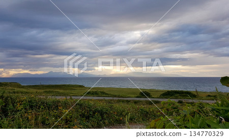 Evening coastal view on the Kuril Islands. Rolling green hills meet the sea under a dramatic sky. Sunlight streams through the clouds Evening coastal view on the Kuril Islands. Rolling green hills meet the sea under a dramatic sky. Sunlight streams through the clouds 134770329