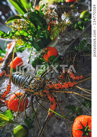 Fresh spiny lobsters on ice at a seafood market with tropical greenery and tomatoes Fresh spiny lobsters on ice at a seafood market with tropical greenery and tomatoes 134770384