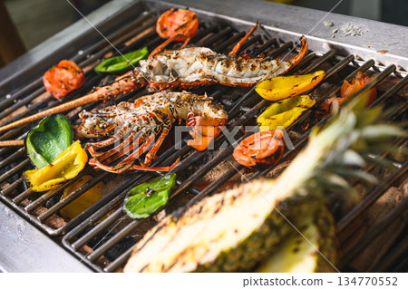 Grilled spiny lobsters with flames, pineapple and vegetables on an open outdoor grill Grilled spiny lobsters with flames, pineapple and vegetables on an open outdoor grill 134770552