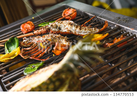 Grilled spiny lobsters with flames, pineapple and vegetables on an open outdoor grill 134770553