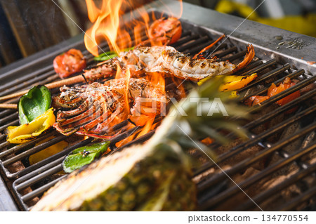 Grilled spiny lobsters with flames, pineapple and vegetables on an open outdoor grill Grilled spiny lobsters with flames, pineapple and vegetables on an open outdoor grill 134770554