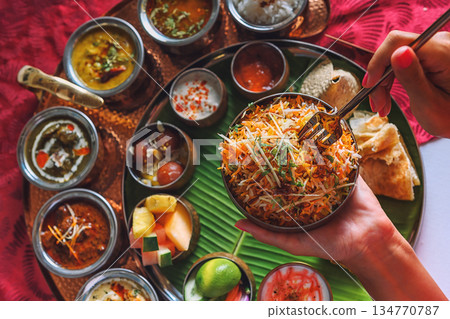 Woman's hand dipping naan bread into traditional Indian curry on a diverse Thali platter 134770787