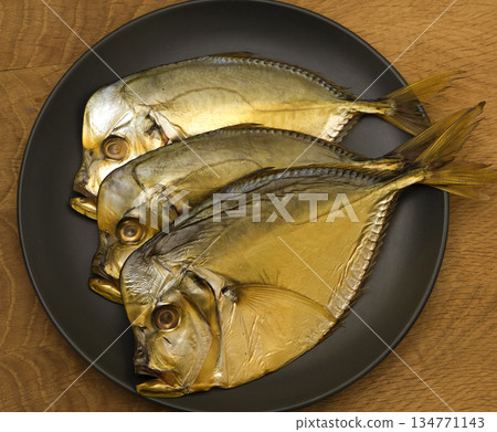 Three smoked vomer fish, lie on a black plate, on a wooden board Three smoked vomer fish, lie on a black plate, on a wooden board 134771143
