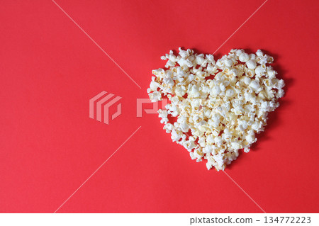 Love cinema concept of popcorn. Heart shaped white fluffy popcorn on red background with empty space for text Love cinema concept of popcorn. Heart shaped white fluffy popcorn on red background with empty space for text 134772223