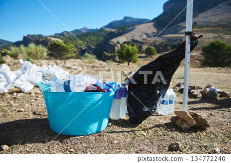 Outdoor Mountain Cleanup Scene With Blue Bucket Of Plastic Bottles And Bagged Waste 134772240