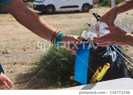 People Refill Water Bottle Outdoors During Camping Trip, Sharing Hydration At A Rural Site 134772246
