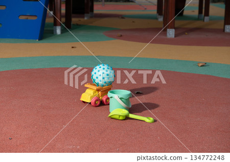 Colorful Playground Toys Ball Bucket Shovel Resting On Soft Rubber Surface In Public Playground Area 134772248