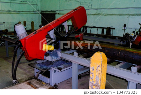 Industrial horizontal band saw cutting large steel pipe in workshop 134772323