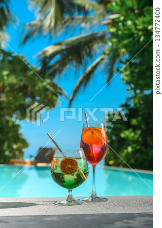 Tropical luxury cocktail with fruits by the pool with palm tree and see background Tropical luxury cocktail with fruits by the pool with palm tree and see background 134772400