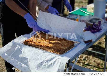 Outdoor Food Prep: People Wearing Gloves Cutting Fresh Baked Pie On Table At A Community Event Outdoor Food Prep: People Wearing Gloves Cutting Fresh Baked Pie On Table At A Community Event 134772429