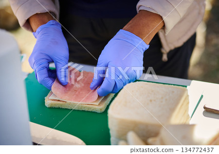 Outdoor Food Prep: Gloves-On Ham Sandwich Assembly on a Green Cutting Board Outdoor Food Prep: Gloves-On Ham Sandwich Assembly on a Green Cutting Board 134772437