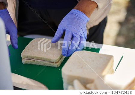 Professional Hands in Purple Gloves Assemble Fresh Sandwiches on Green Cutting Board Professional Hands in Purple Gloves Assemble Fresh Sandwiches on Green Cutting Board 134772438
