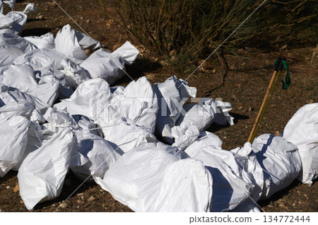 White Garbage Bags Piled On Ground With Cleanup Tools In Outdoor Area White Garbage Bags Piled On Ground With Cleanup Tools In Outdoor Area 134772444