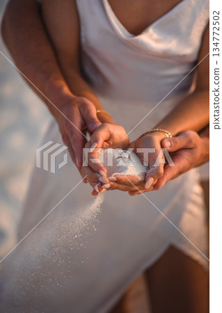 Romantic engagement on the beach: Couple holding white sand with a diamond ring during sunset Romantic engagement on the beach: Couple holding white sand with a diamond ring during sunset 134772502
