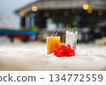 Tropical beach cocktails and red hibiscus flower on white sand with blurred resort background 134772559