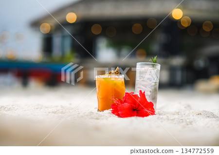 Tropical beach cocktails and red hibiscus flower on white sand with blurred resort background 134772559