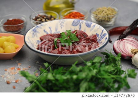 Cut raw beef liver with onions, spices, chili peppers and dill on wooden table, flat lay Cut raw beef liver with onions, spices, chili peppers and dill on wooden table, flat lay 134772676