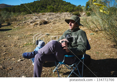 Relaxed Photographer Sitting in Camping Chair Outdoors With Camera in Sunny Natural Setting Relaxed Photographer Sitting in Camping Chair Outdoors With Camera in Sunny Natural Setting 134772700