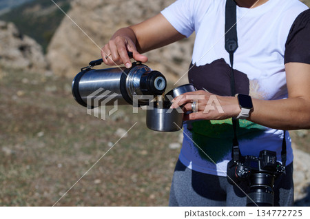 Outdoor Adventure Woman Pouring Coffee From Thermos Into Cup During Hiking With Camera Outdoor Adventure Woman Pouring Coffee From Thermos Into Cup During Hiking With Camera 134772725