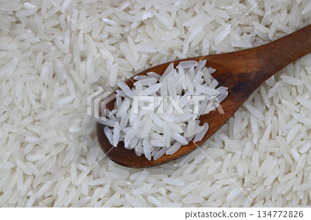 Raw white rice on wooden background. Long uncooked rice in wooden plate. Natural organic food. Traditional Asian cereal culture. 134772826