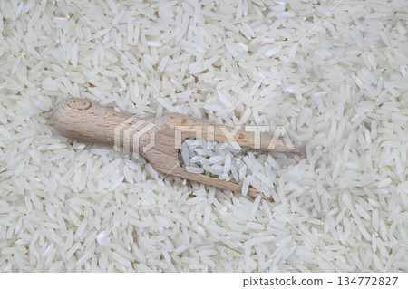 Raw white rice on wooden background. Long uncooked rice in wooden plate. Natural organic food. Traditional Asian cereal culture. Raw white rice on wooden background. Long uncooked rice in wooden plate. Natural organic food. Traditional Asian cereal culture. 134772827