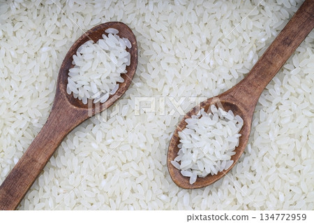 Raw white rice on wooden background. Long uncooked rice in wooden plate. Natural organic food. Traditional Asian cereal culture. Raw white rice on wooden background. Long uncooked rice in wooden plate. Natural organic food. Traditional Asian cereal culture. 134772959
