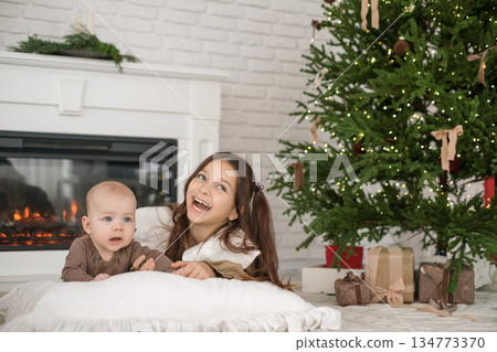 Funny laughing children on the floor in front of the fireplace, next to the Christmas tree. Looking forward to Christmas and New Year Funny laughing children on the floor in front of the fireplace, next to the Christmas tree. Looking forward to Christmas and New Year 134773370