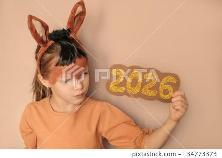 The sly girl stares intently at the shiny numbers of 2026. A child in the form of a fiery horse is a symbol of the Chinese New Year calendar 134773373