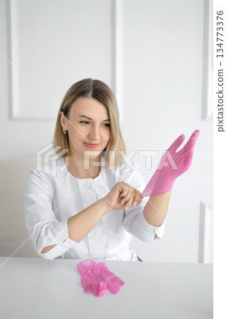 A female medical worker puts on pink latex gloves. 134773376