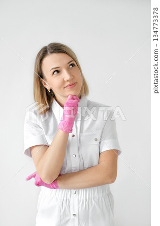 A thoughtful female doctor in pink gloves is thinking while looking away. A nurse on a white studio background 134773378