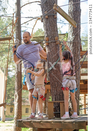 A father helps his daughter install a carabiner on the rope of a suspended rope amusement park. Rock climbing skills training A father helps his daughter install a carabiner on the rope of a suspended rope amusement park. Rock climbing skills training 134773411