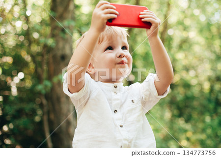 Young boy outdoors lifts a red tablet, capturing a bright moment of childhood Young boy outdoors lifts a red tablet, capturing a bright moment of childhood 134773756