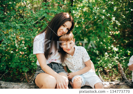A loving mother sits with her two sons outdoors, sharing a warm, everyday moment of family bonding and togetherness A loving mother sits with her two sons outdoors, sharing a warm, everyday moment of family bonding and togetherness 134773770