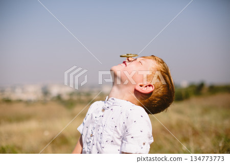 Child balances a spinning toy on his nose in a sunny open field 134773773