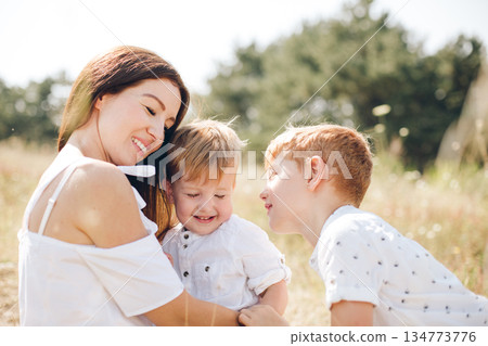 Mother and her two sons share a joyful moment in a sunlit outdoor field Mother and her two sons share a joyful moment in a sunlit outdoor field 134773776