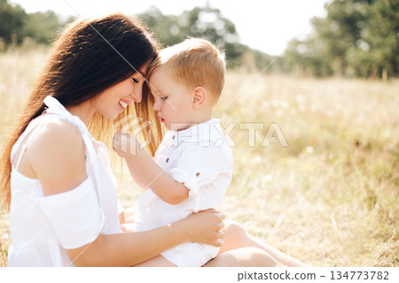 Mother and her two sons share a tender moment in a sunny outdoor field Mother and her two sons share a tender moment in a sunny outdoor field 134773782